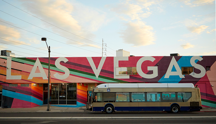 _AP_3417 1 A public bus is parked in front of a colorful mural with large letters spelling “LAS VEGAS” on the side of a building under a partly cloudy sky.
