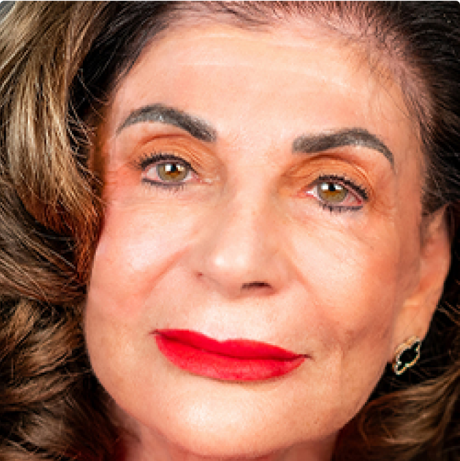 image-3 Close-up of an older woman with wavy brown hair, bold red lipstick, well-groomed eyebrows, and gold hoop earrings, looking directly at the camera with a neutral expression.