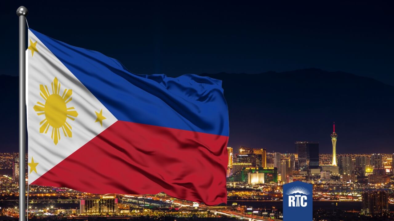 A Philippine flag waves prominently in the foreground, with a brightly lit city skyline at night in the background. The RTC logo is visible in the lower right corner.
